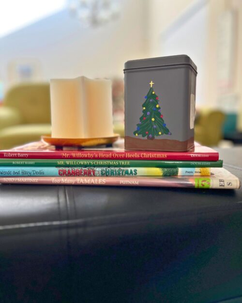a painted tea tin on a stack of christmas books with a candle.
