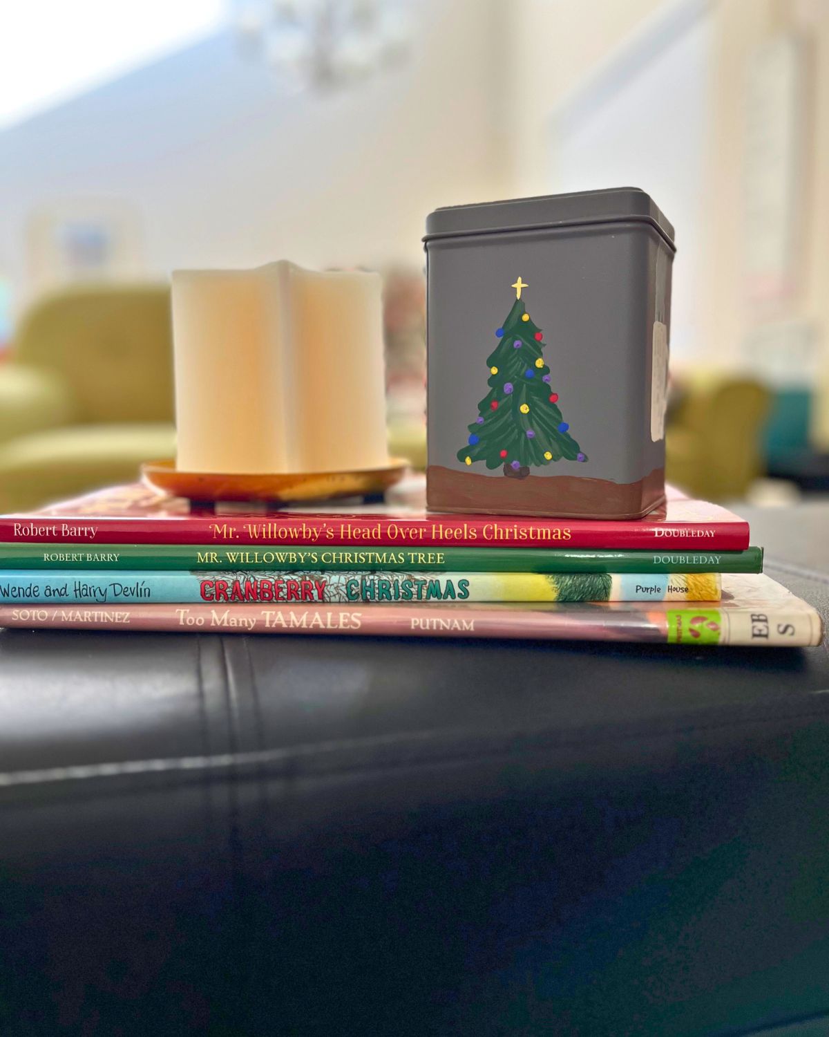 a painted tea tin on a stack of christmas books with a candle.