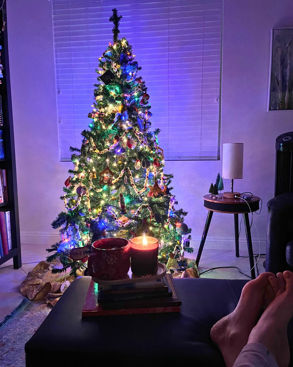 feet propped on ottoman in front of lit christmas tree.
