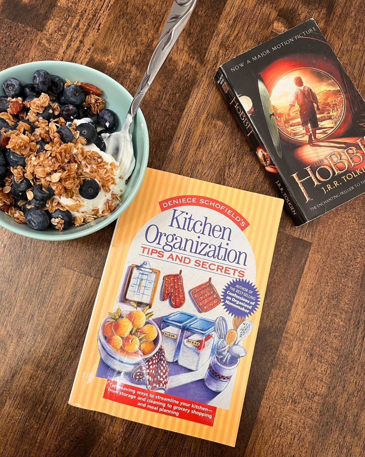 bowl of yogurt, blueberries, and granola next to books on table.