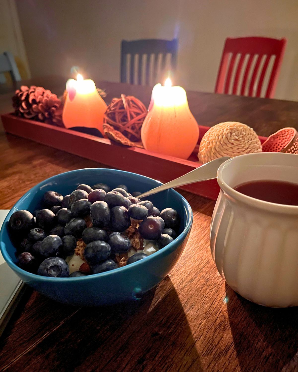 candles lit in background with bowl of blueberries and cup of tea in foreground.