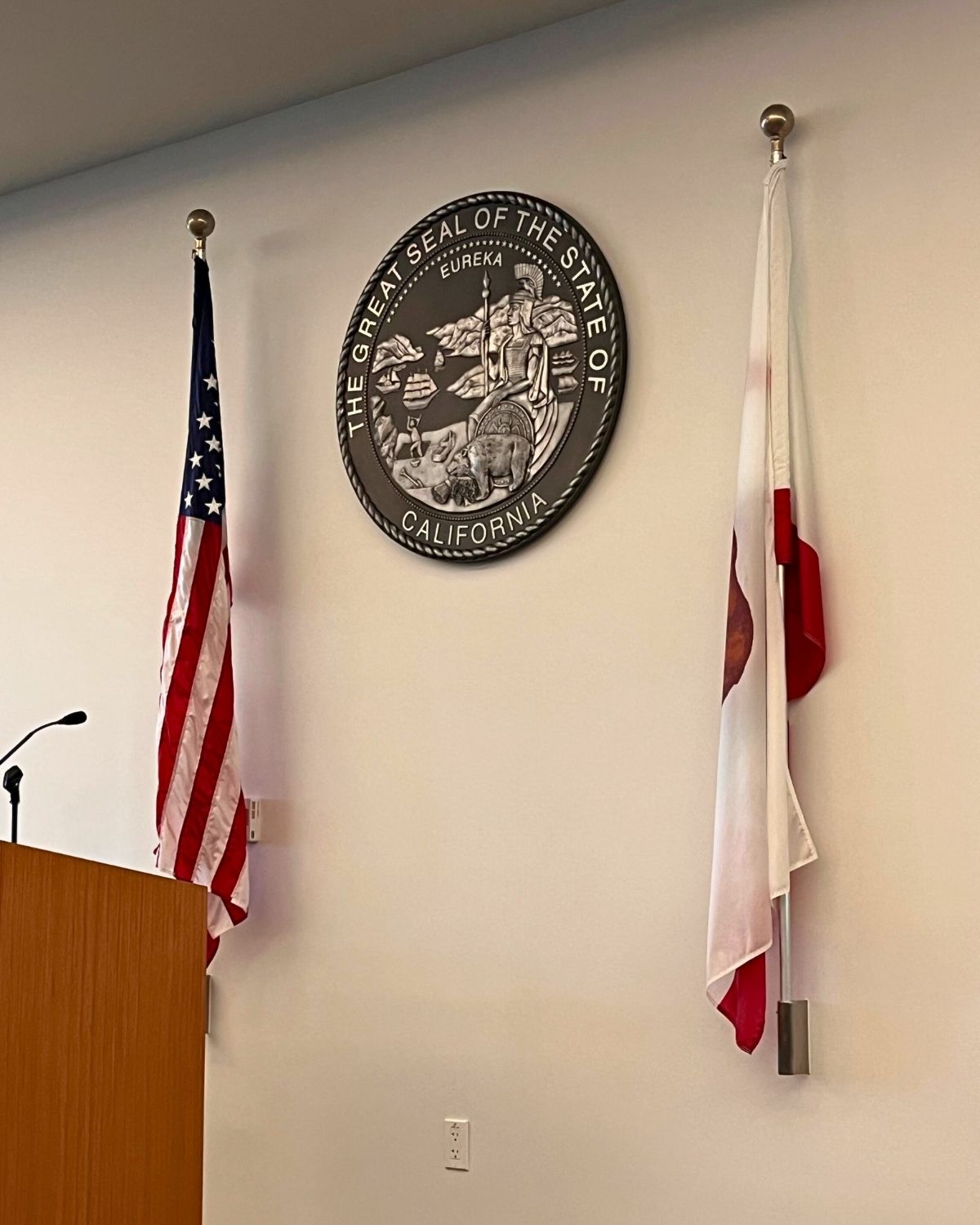 podium, us and state flag, with the great seal of ca on wall.