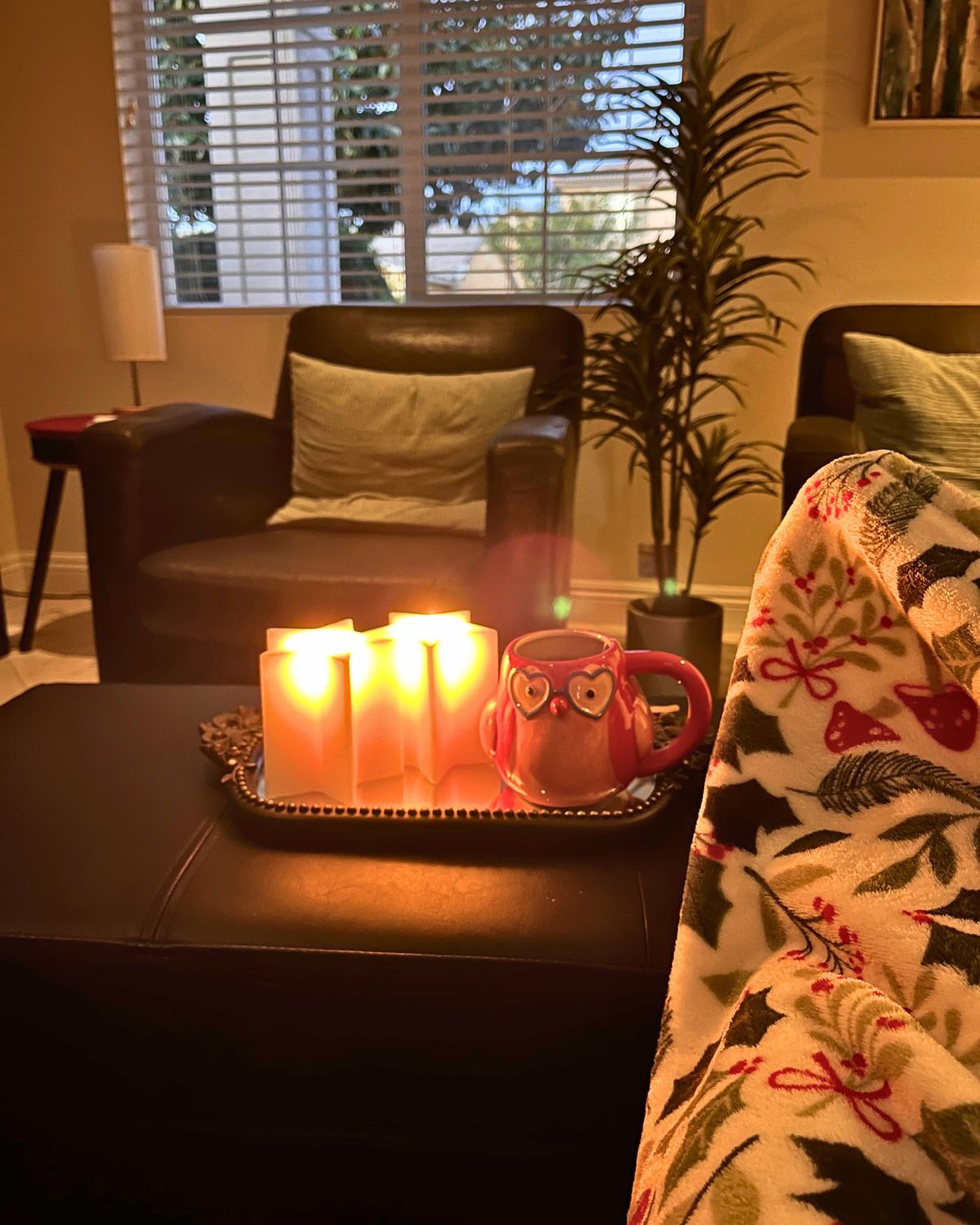 lit star candles with owl mug on ottoman, feet propped up under blanket nearby.
