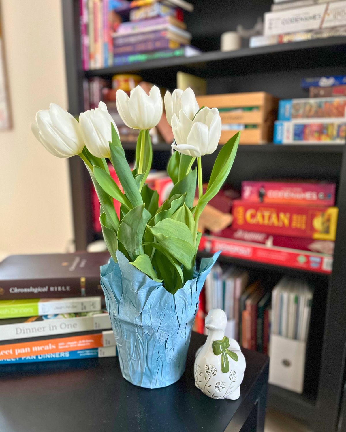 tulips on table with books and ceramic duck, with bookshelf behind.