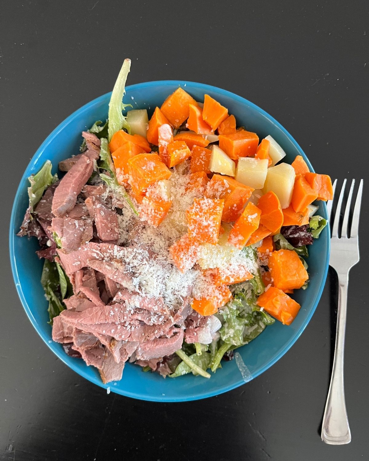 blue plate of caesar salad, homemade roast beef, and potato cubes.