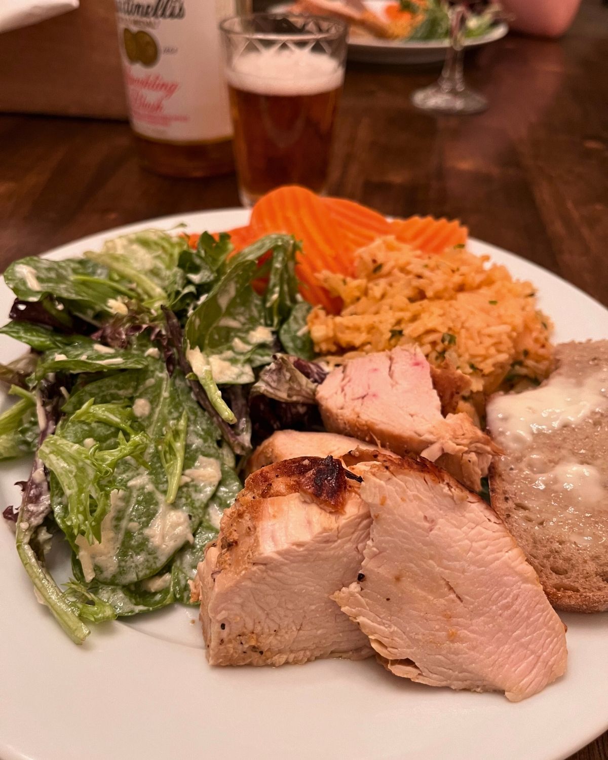 sunday dinner plate: caesar salad, rice, carrots, bread, and chicken.
