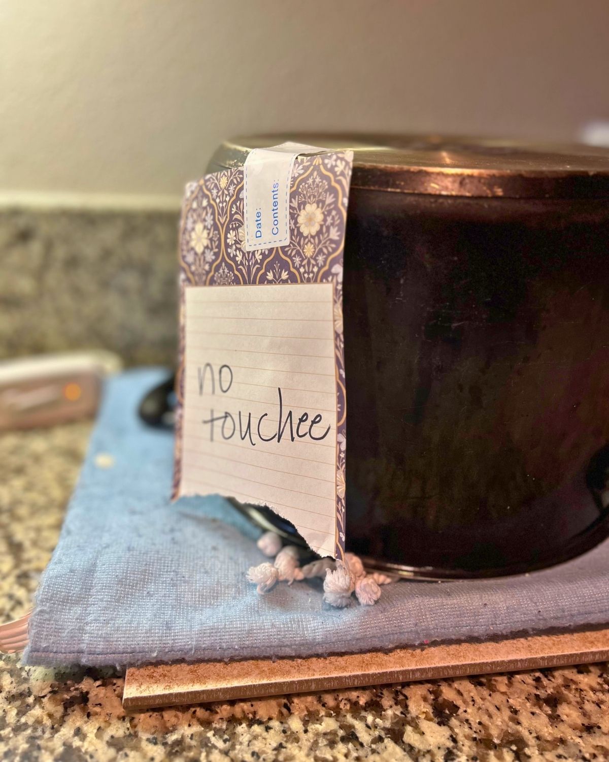 stockpot inverted on heating pad with a no touch sign taped to it.