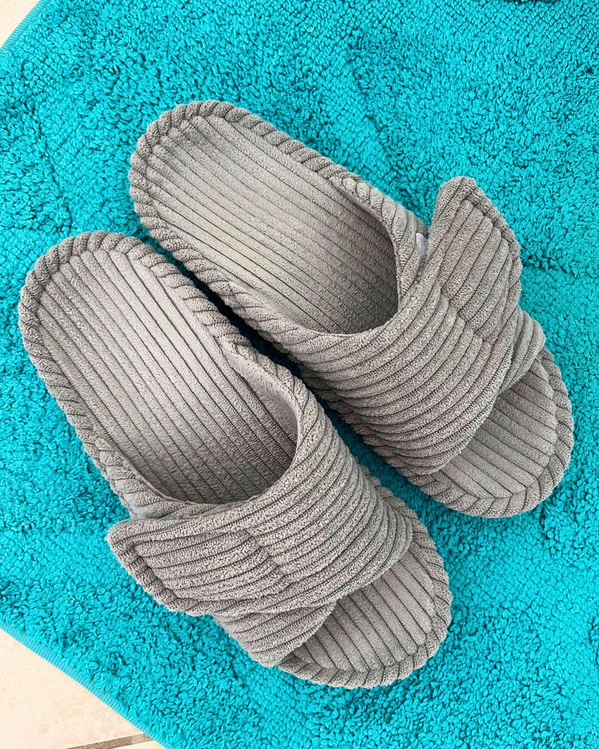 gray house shoes on teal mat on tile floor.