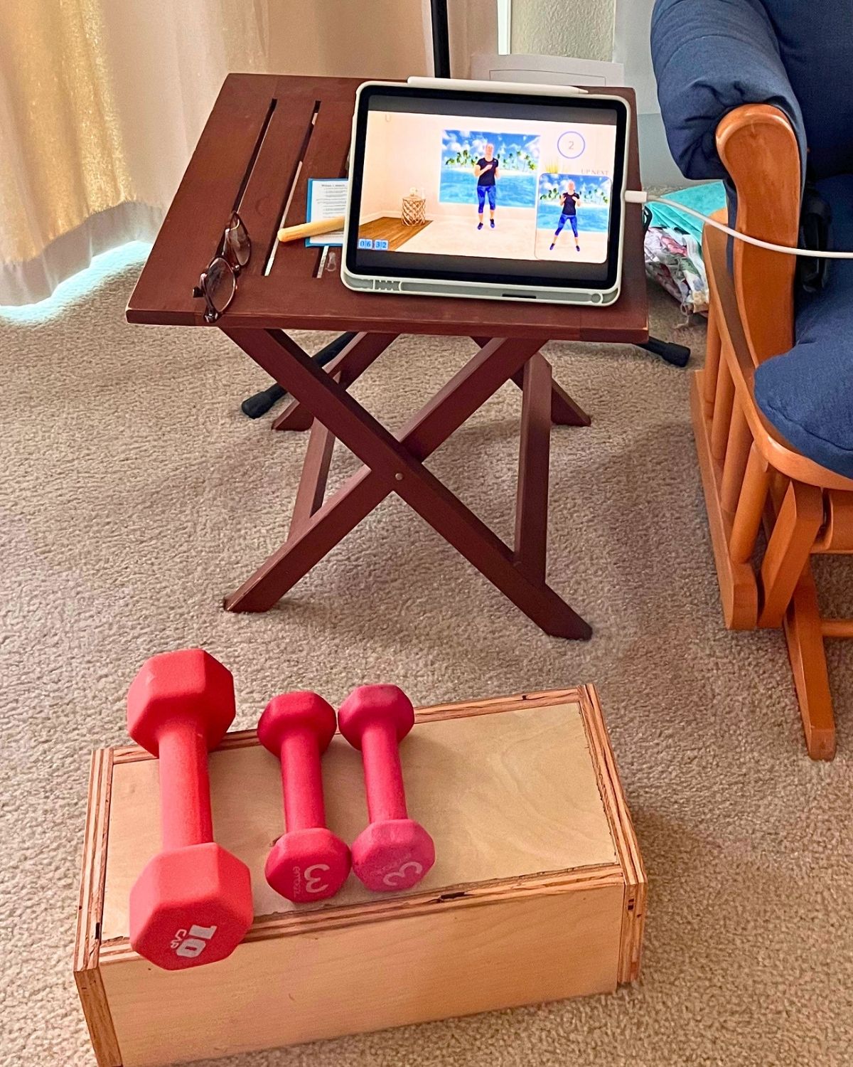 workout video on iPad on table with weights sitting on block on floor.