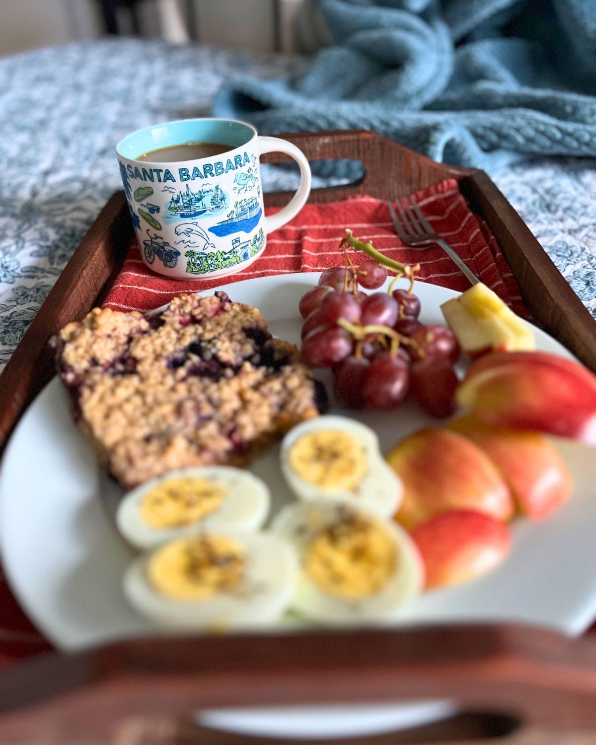 breakfast tray on bed loaded with fruit, eggs, and baked oatmeal.