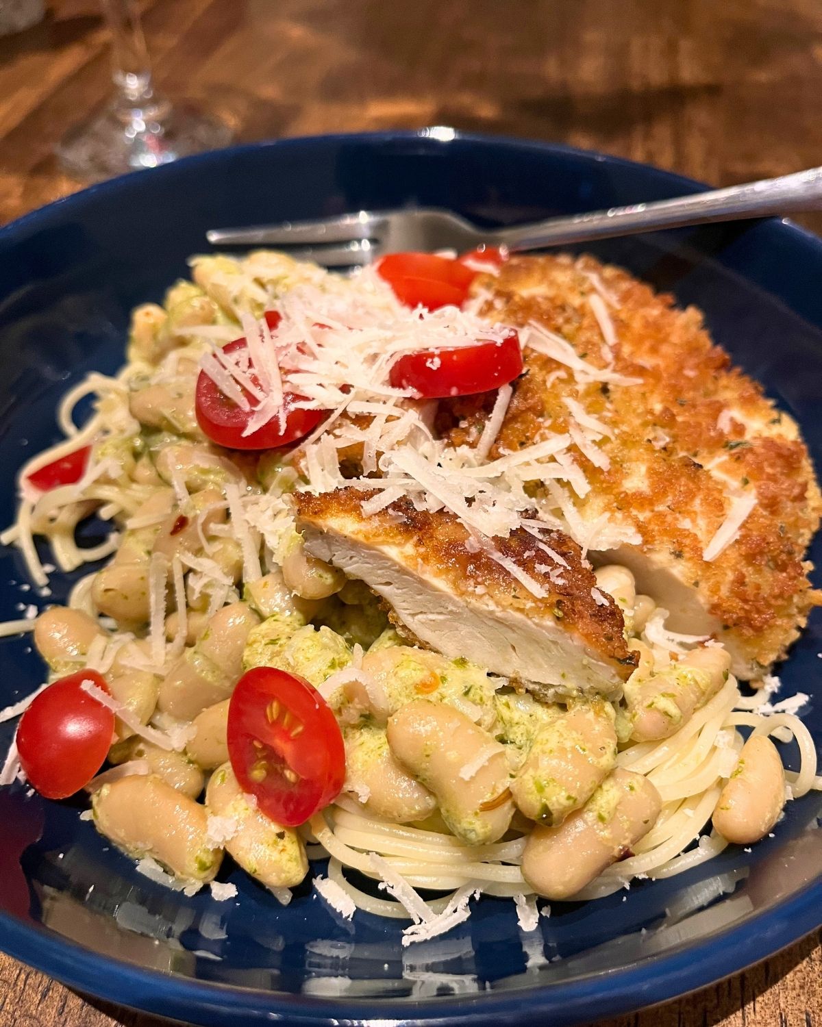 dark blue plate of chicken and pesto beans on pasta.