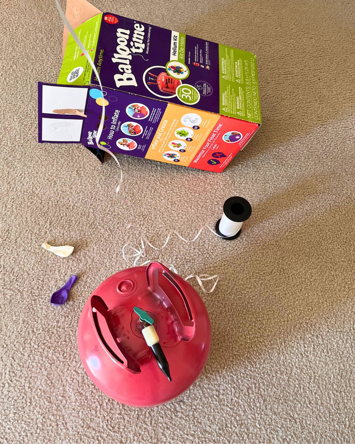 helium balloon tank on carpet with scissors, balloons, and ribbon.