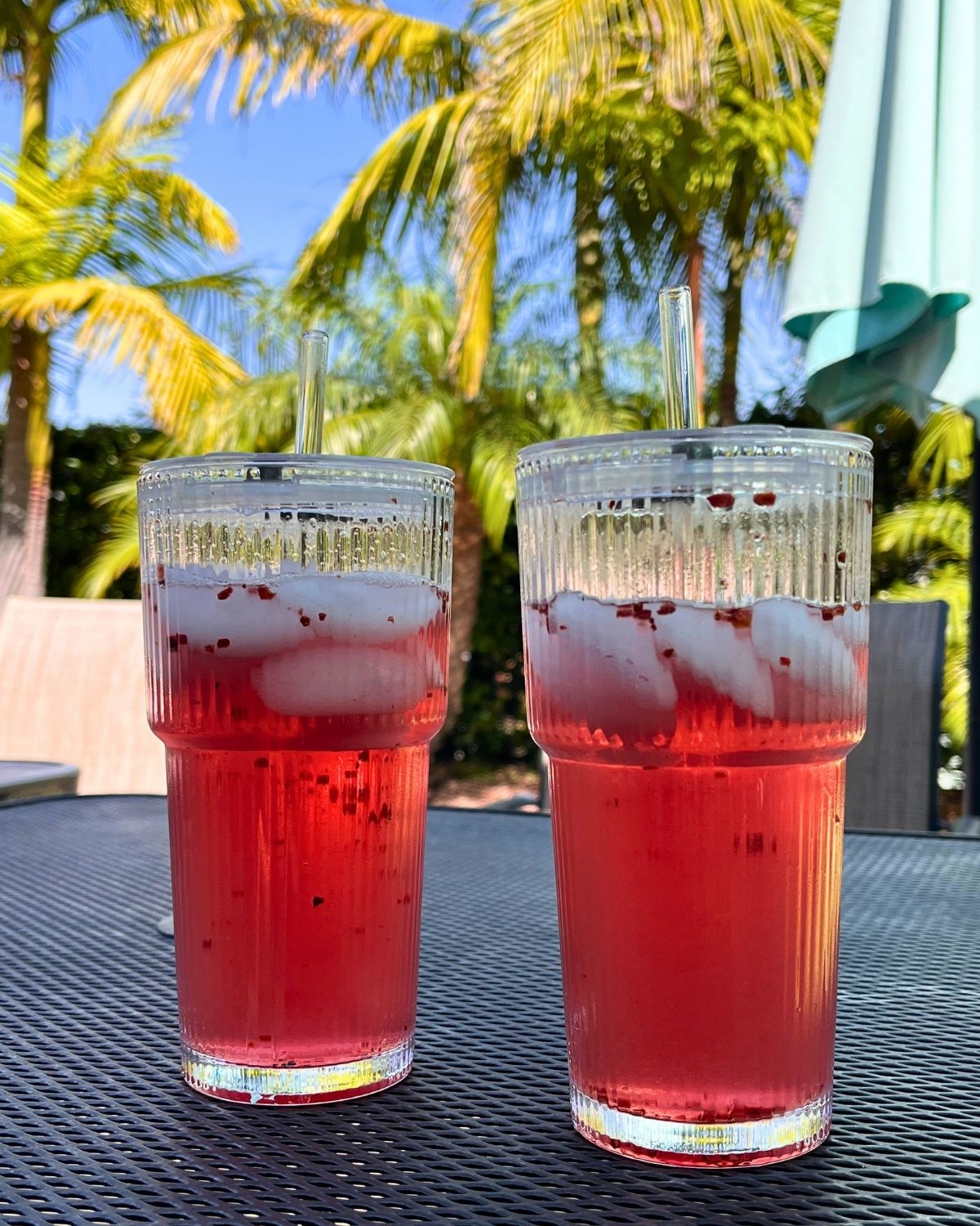 two clear glasses of iced tea with palm trees in the background.