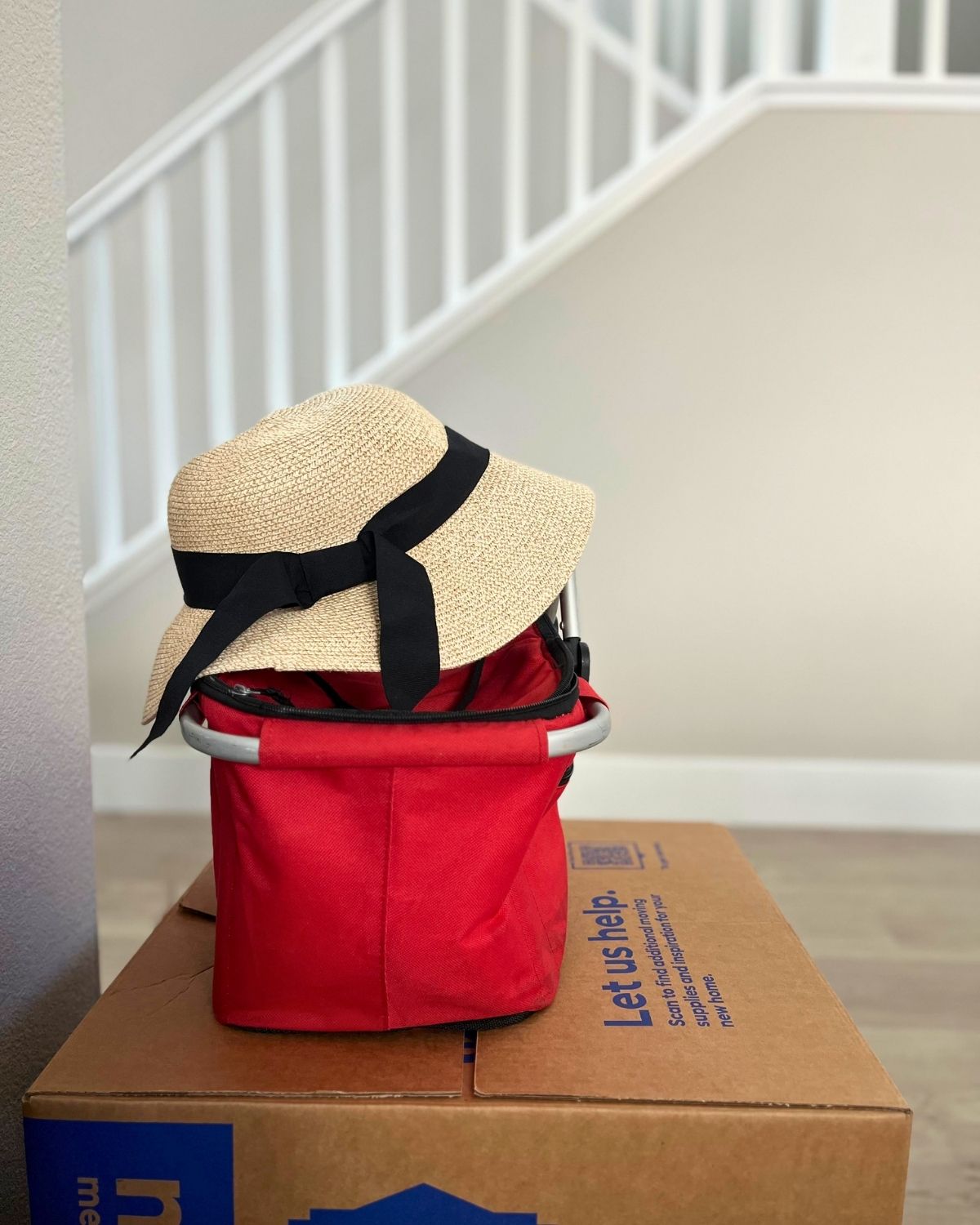 sunhat atop red cooler atop moving box with stairwell in the background.