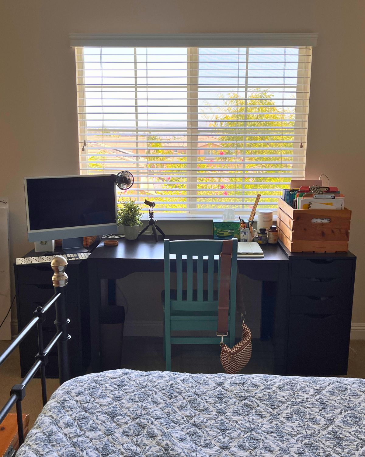 bed made in foreground with clean desk in front of open window in background.