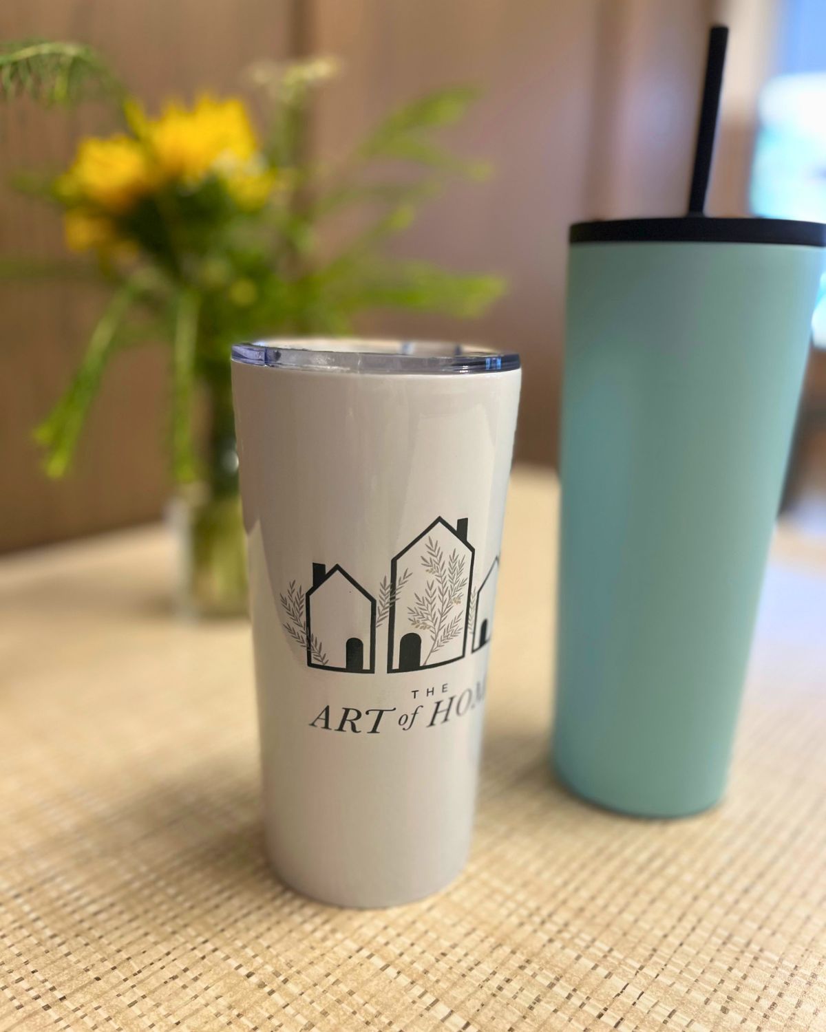 table with vase of yellow flowers, art of home tumbler and water tumbler.