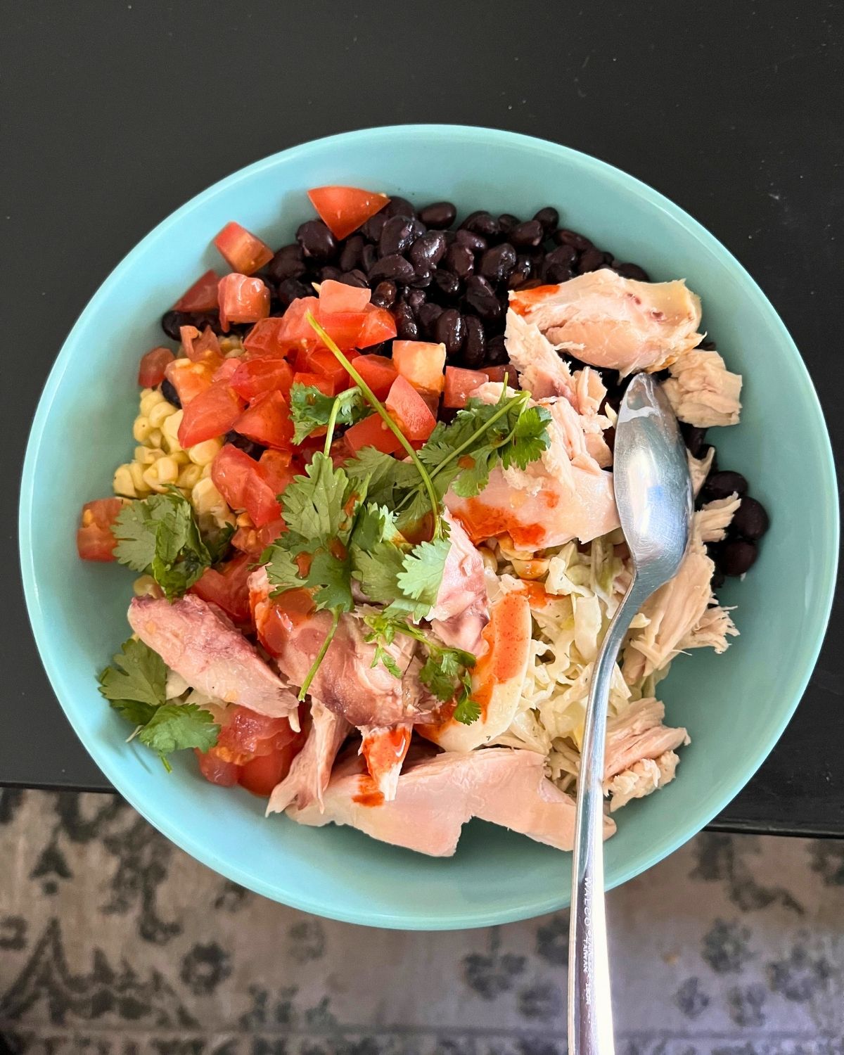 protein lunch in a teal bowl on a black table with a rug underneath.