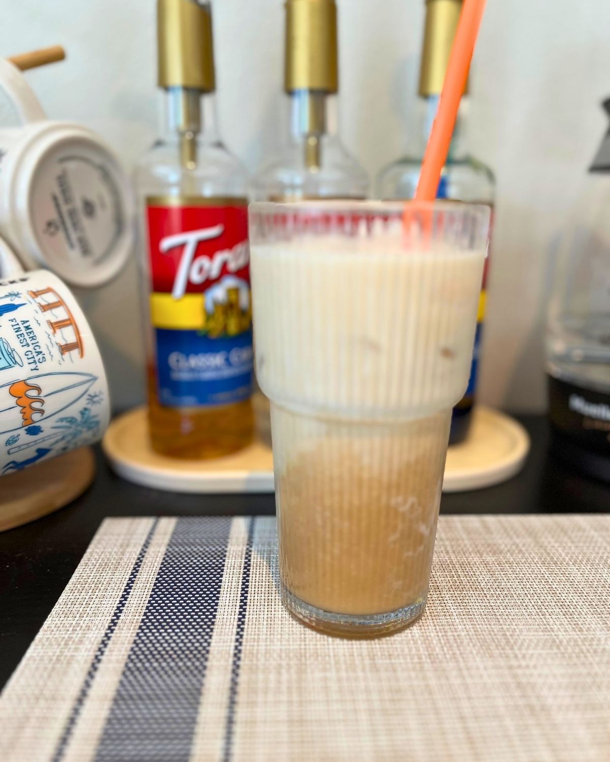 protein latte in glass with syrups lined up in background.