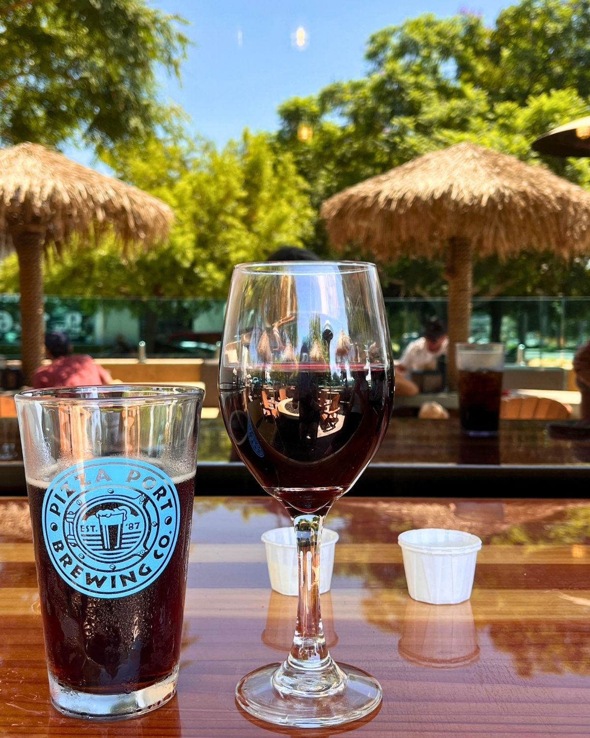 pint of beer from pizza port next to a wine glass on the patio with palm fronds in the background.