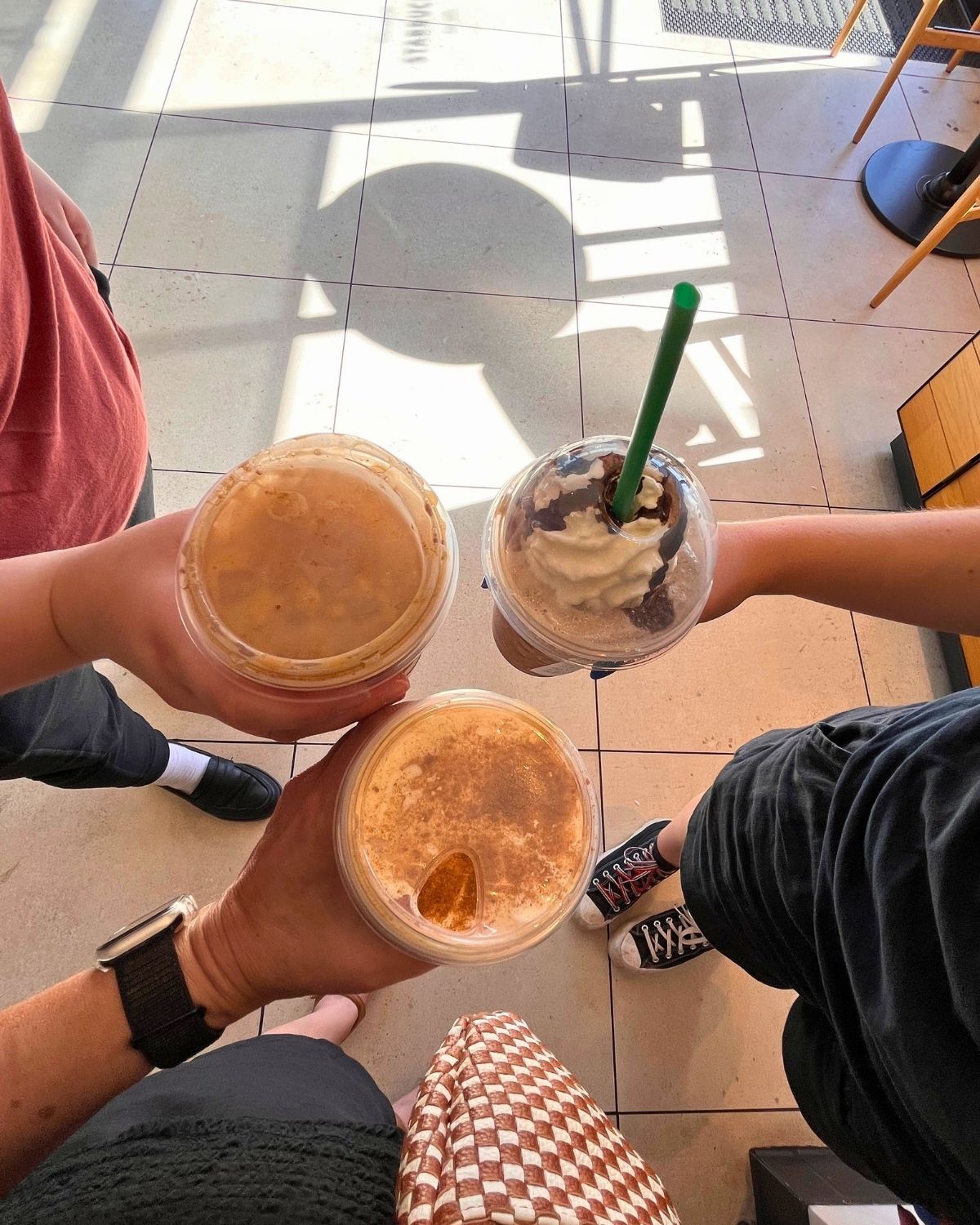 three women holding coffee drinks over their feet.