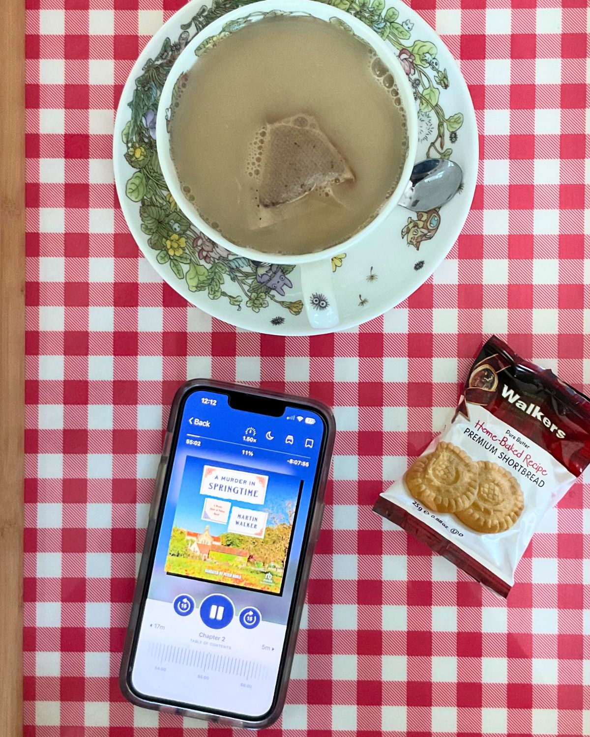 tea cup on tray with packet of shortbread and an audio book cued up on iPhone.