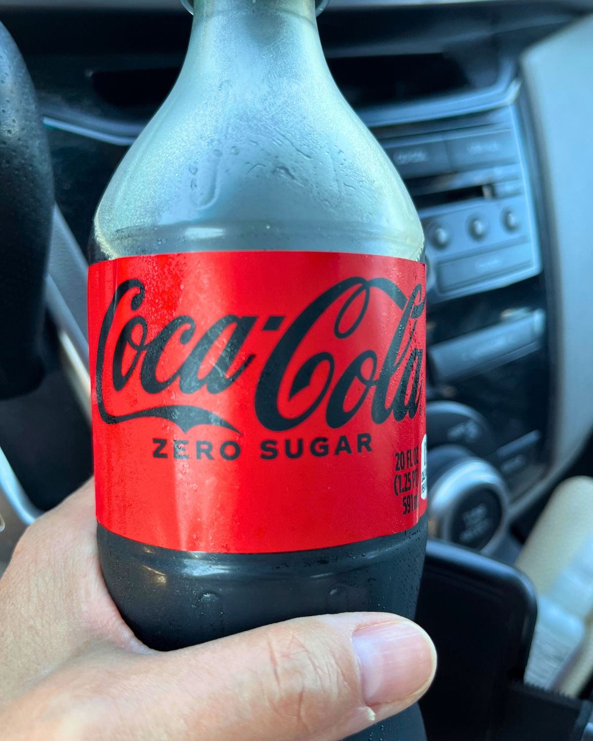 holding a bottle of coke zero in the car.